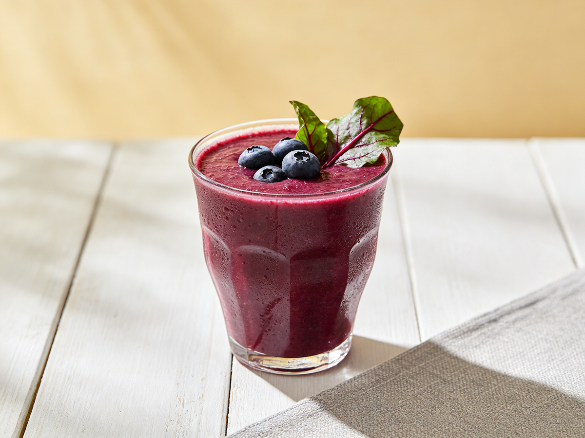 Fresh homemade beet berry antioxidant juice made with beets blueberries strawberries apple and lemon served in a clear glass on a marble kitchen countertop